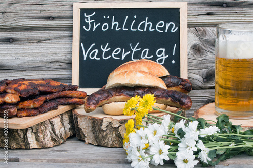Tafel mit Text "Fröhlichen Vatertag" mit Bier-Bratwurst und Bauchfleisch rustikal vor Holzhintergrund
