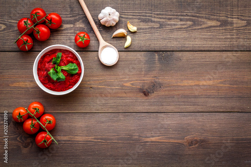 Homemade tomato ketchup with cherry tomatoes, garlic and basil on dark wooden background top view space for text