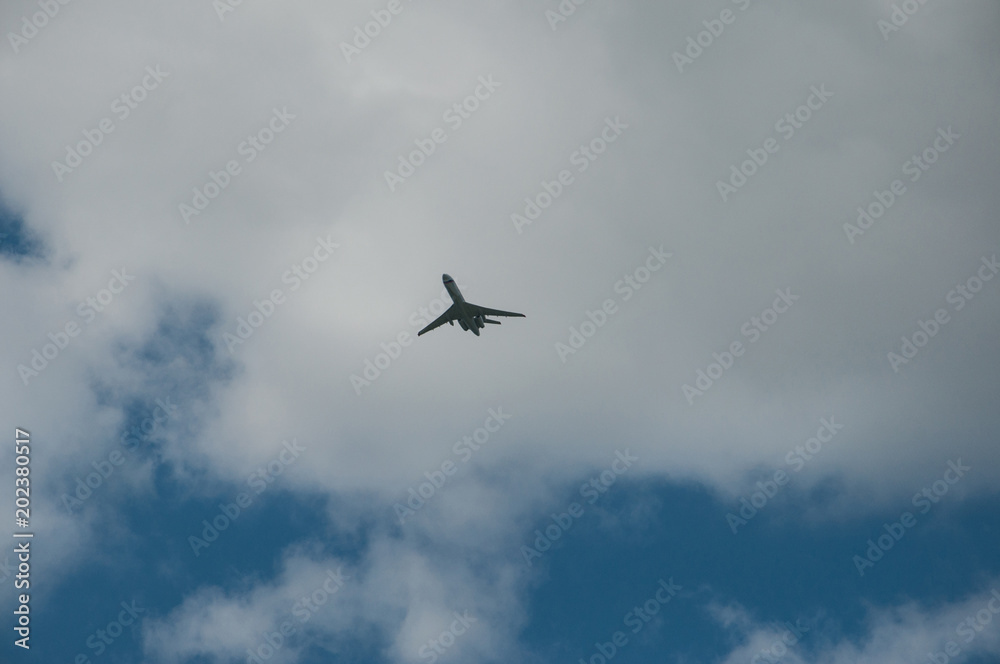 a passenger plane flies against the backdrop of blue sky and gray cloud