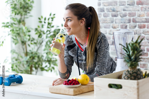 Sporty young woman looking sideways while drinking lemon juice in the kitchen at home. photo