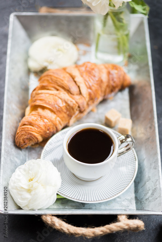 Fresh Croissant, Cup of Coffee and Ranunculus Flowers. Breakfast