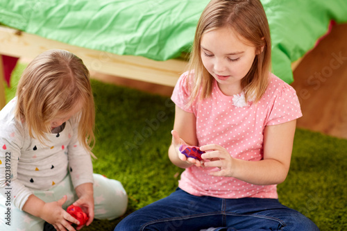 childhood, leisure and people concept - girls or sisters with modelling clay or slimes at home