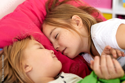 childhood, bedtime and family concept - happy little girls or sisters sleeping in bed at home