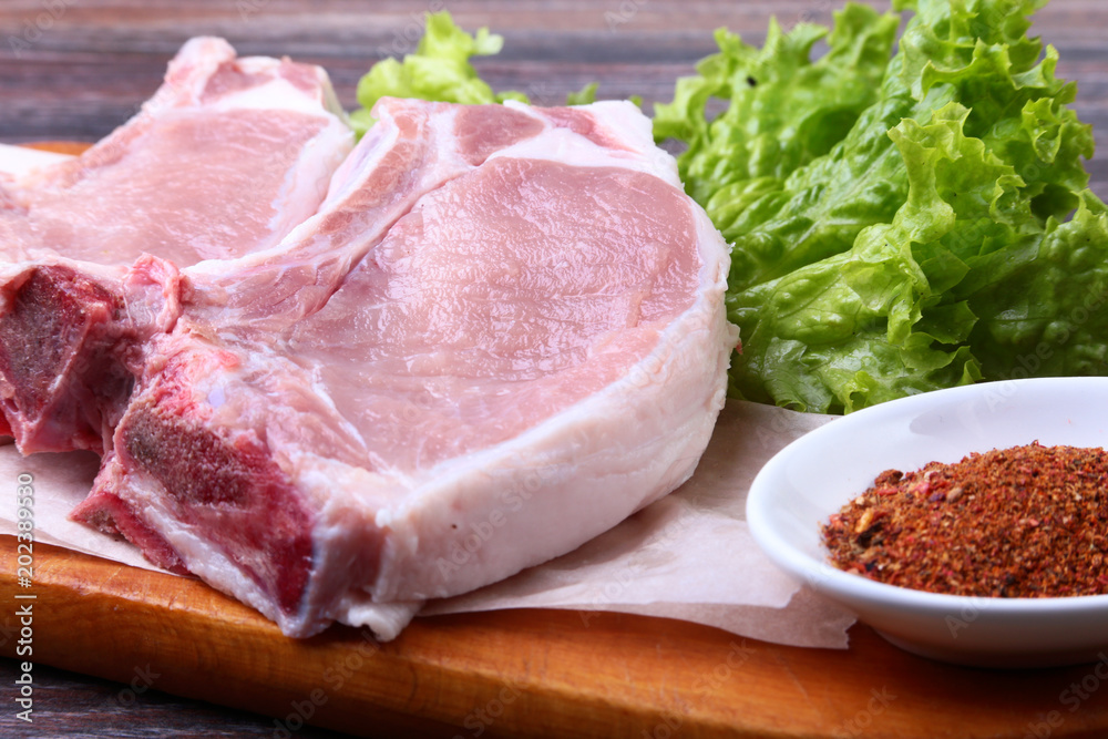 Raw pork steak with spices Leaves lettuce on wooden cutting board. Ready for cooking. Raw pork steak with spices Leaves lettuce on wooden cutting board. Ready for cooking.