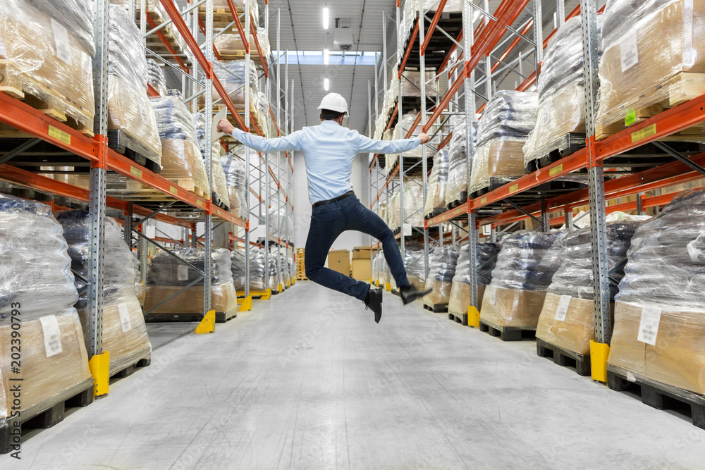 logistic business, success and people concept - happy businessman in helmet jumping at warehouse - obrazy, fototapety, plakaty 