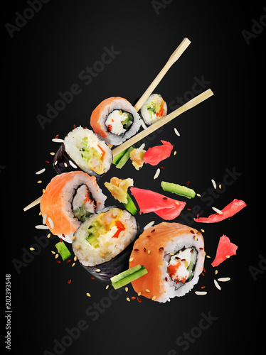 Different fresh sushi rolls with chopsticks frozen in the air on black background