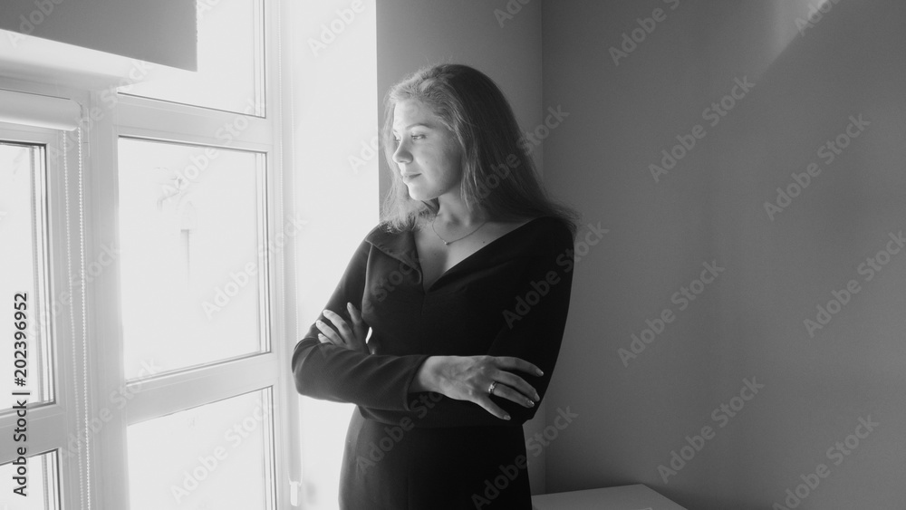 Black and white image of young elegant woman looking out of big window Black and white image of young elegant woman looking out of big window