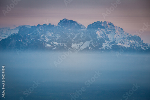 Sunrise on snow-covered Mount Schiara peaks dipped in the mist, Dolomites, Veneto, Italy
