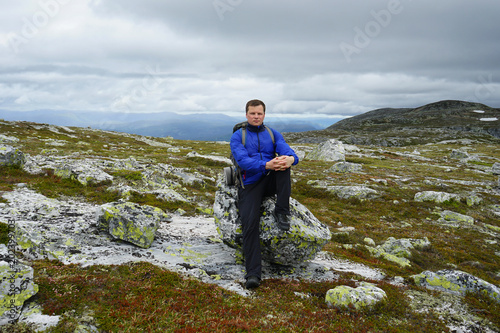 Young man with backpack sits on a rock.