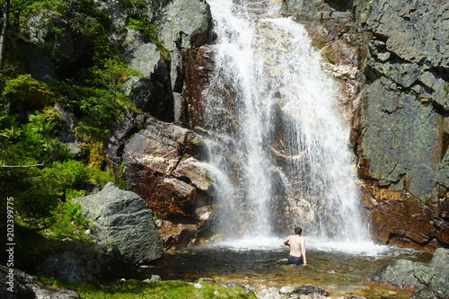 Man walking into the waterfall alone. Travel Lifestyle adventure concept of an active vacations into the wild nature.