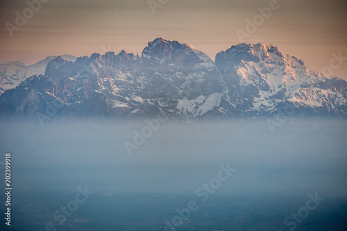 Sunrise on snow-covered Mount Schiara peaks dipped in the mist, Dolomites, Veneto, Italy photo