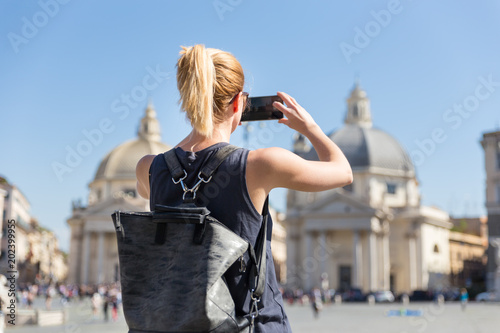 Female tourist with a fashinable vintage hipster backpack taking photo oof Piazza del Popolo, People's Square, in Rome, Italy by her mobile phone.