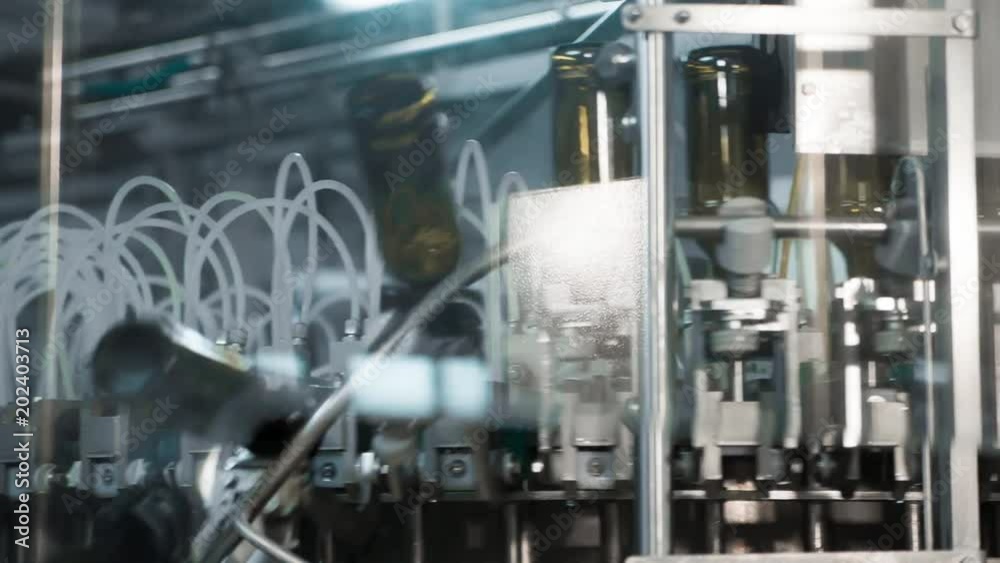 Automatic filling machine pouring beer in a brewery. Glass bottles for beer on the conveyor belt. Filling machine for industry. Automatic filling machine pouring beer in a brewery. Glass bottles for beer on the conveyor belt. Filling machine for industry.