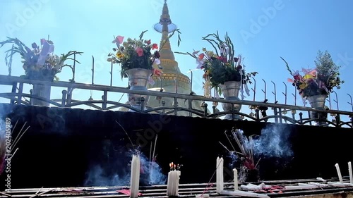 Altar with Buddhist religious offerings - flowers, candles and incense sticks, the golden top of Kyaiktiyo Pagoda on giant golden granite boulder is seen on background, Kyite Htee Yoe Mount, Myanmar. photo