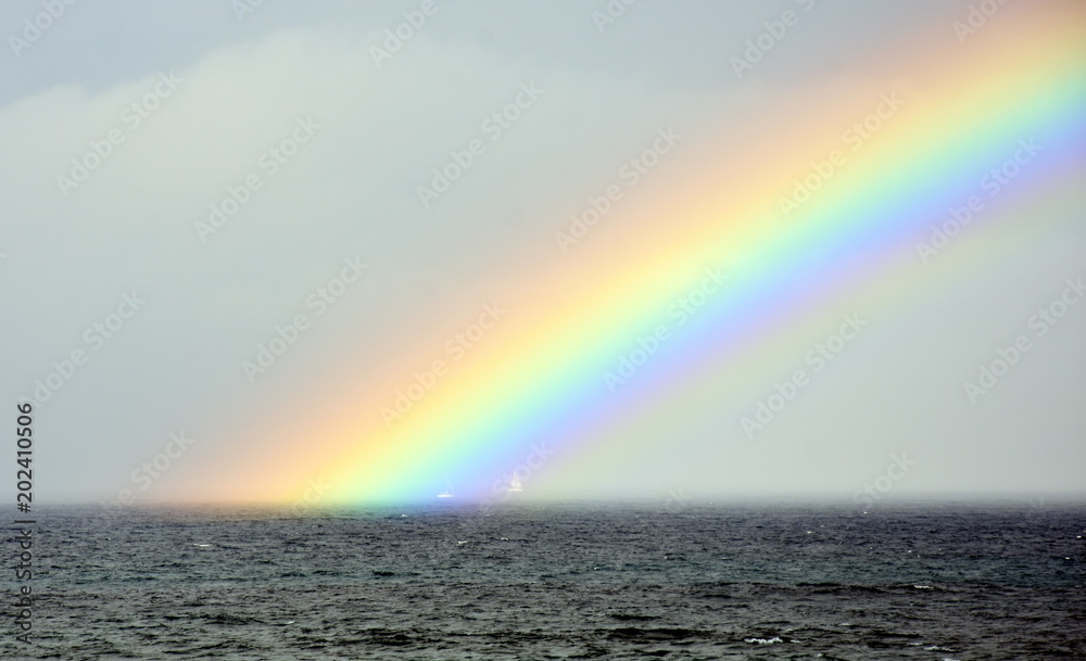 Rainbow over the sea. Seascape with beautiful multicoloured rainbow over the sea. White sailing boat in the background.