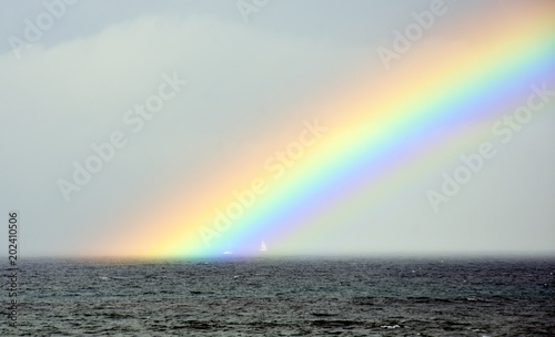 Rainbow over the sea. Seascape with beautiful multicoloured rainbow over the sea. White sailing boat in the background.