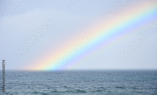 Rainbow over the sea. Seascape with beautiful multicoloured rainbow over the sea. White sailing boat in the background. © katacarix