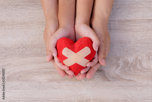 Health care, love, organ donation, family insurance and CSR concept. adult and child hands holding handmade red heart on wooden background.
