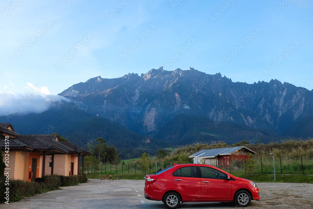 A vibrant red car and house in front of majestic view of Mount Kinabalu at Desa Cattle Dairy Farm