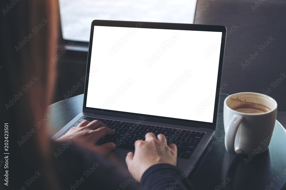 Mockup image of business woman using and typing on laptop with blank white screen and coffee cup on table in cafe Mockup image of business woman using and typing on laptop with blank white screen and coffee cup on table in cafe