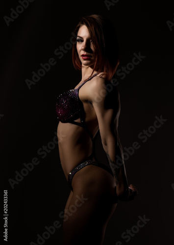 beautiful fitness woman, muscular girl poses on dark background. female body-building