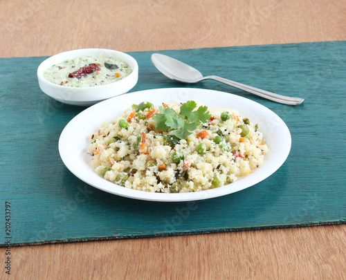 Rice upma, a south Indian vegetarian breakfast made from shredded rice and vegetables, with coconut chutney as a side dish. photo