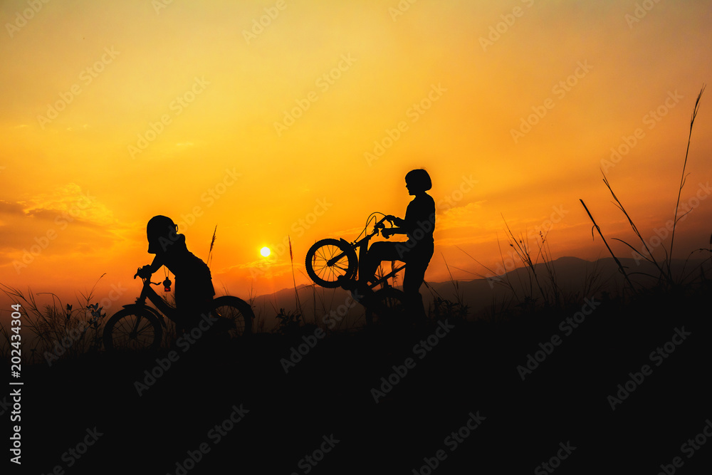Silhouette children playing whit bicycle at sunset background