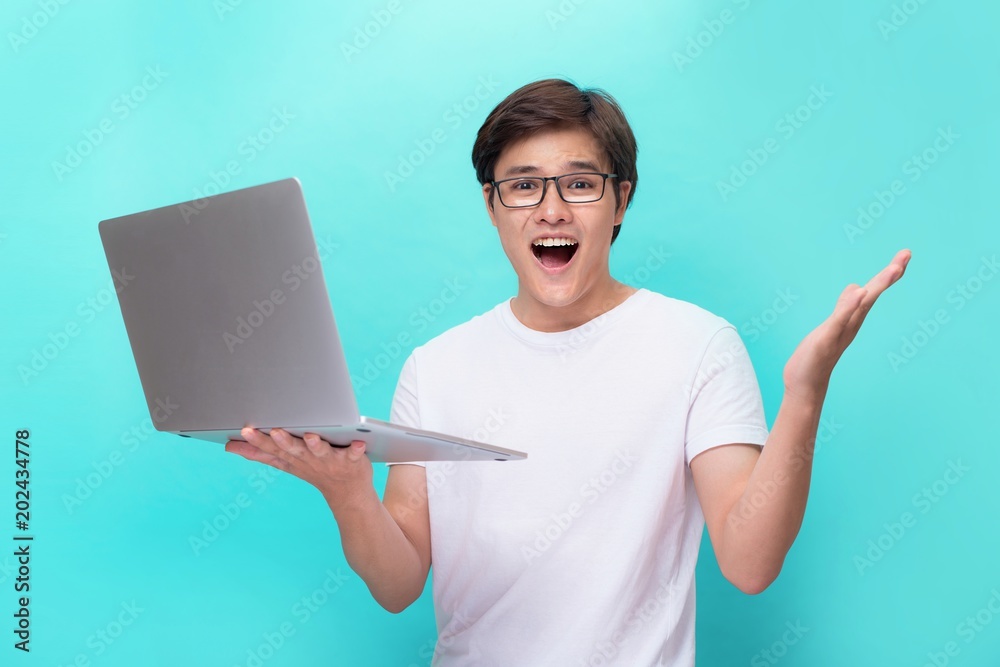 Φωτογραφία A happy excited young asian man with a laptop and showing a fist of success