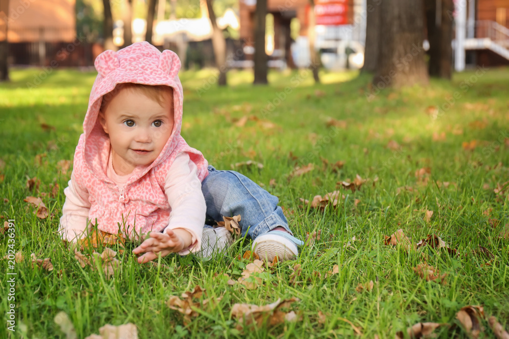 Adorable little girl sitting on grass in autumn park Adorable little girl sitting on grass in autumn park