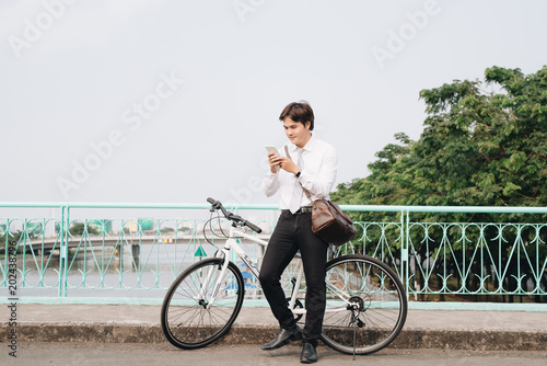 Fototapeta Naklejka Na Ścianę i Meble -  Young handsome guy on a bicycle looking at mobile phone.