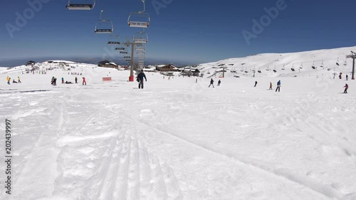 4K. A snowboarder is walking the snowy mountain, passes near the camera and continues. There is a chairlift nearby. Ski resort in Sierra Nevada, Spain-Adrian.