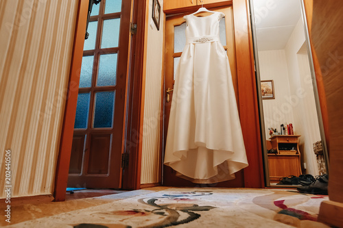 A wedding dress hanging in a doorway in a room on a brown background. Family, marriage, holiday, celebration, wedding.