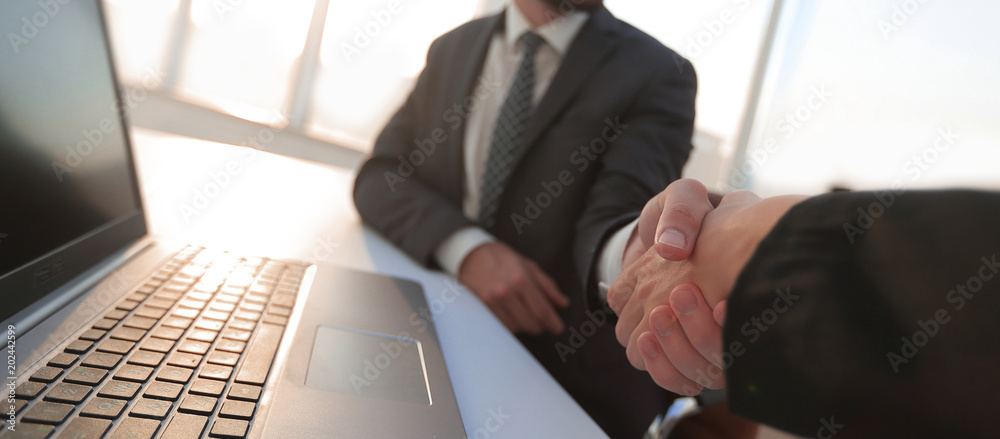 Business partners handshaking over business objects on workplace Business partners handshaking over business objects on workplace