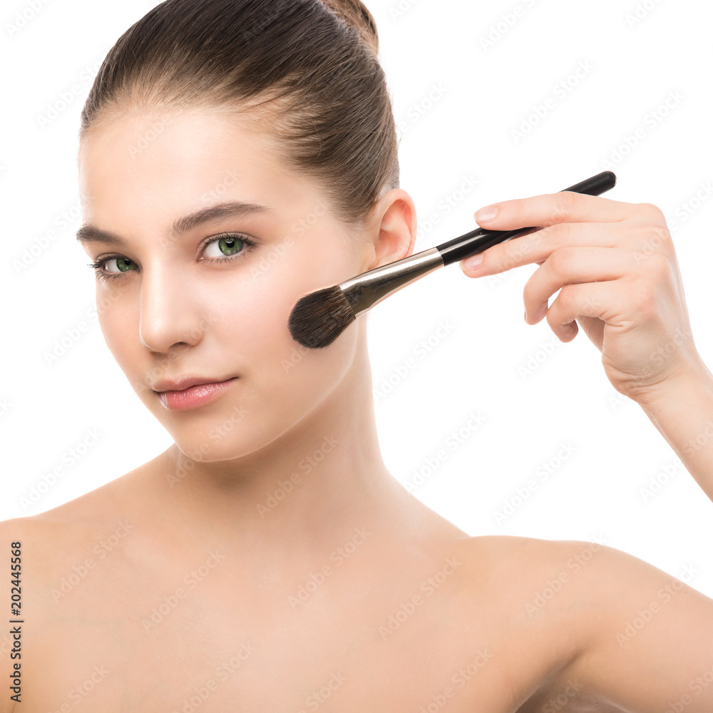 Portrait of beautiful young brunette woman with clean face. Beauty spa model girl with perfect fresh clean skin applying cosmetic brush. Youth and skin care concept. Isolated on a white background.