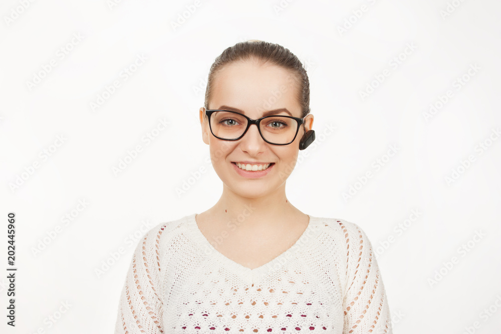 beautiful blonde girl speaks on the phone through a bluetooth earpiece on a white background. emotionally speaking girl in glasses with gathered hair speaks on the phone