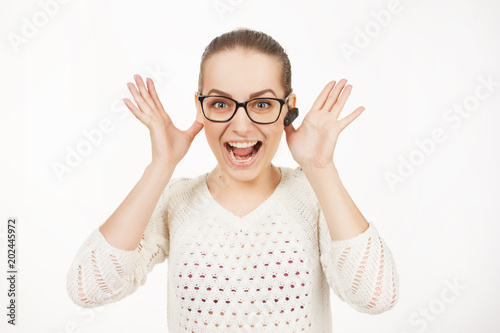 beautiful blonde girl speaks on the phone through a bluetooth earpiece on a white background. emotionally speaking girl in glasses with gathered hair speaks on the phone