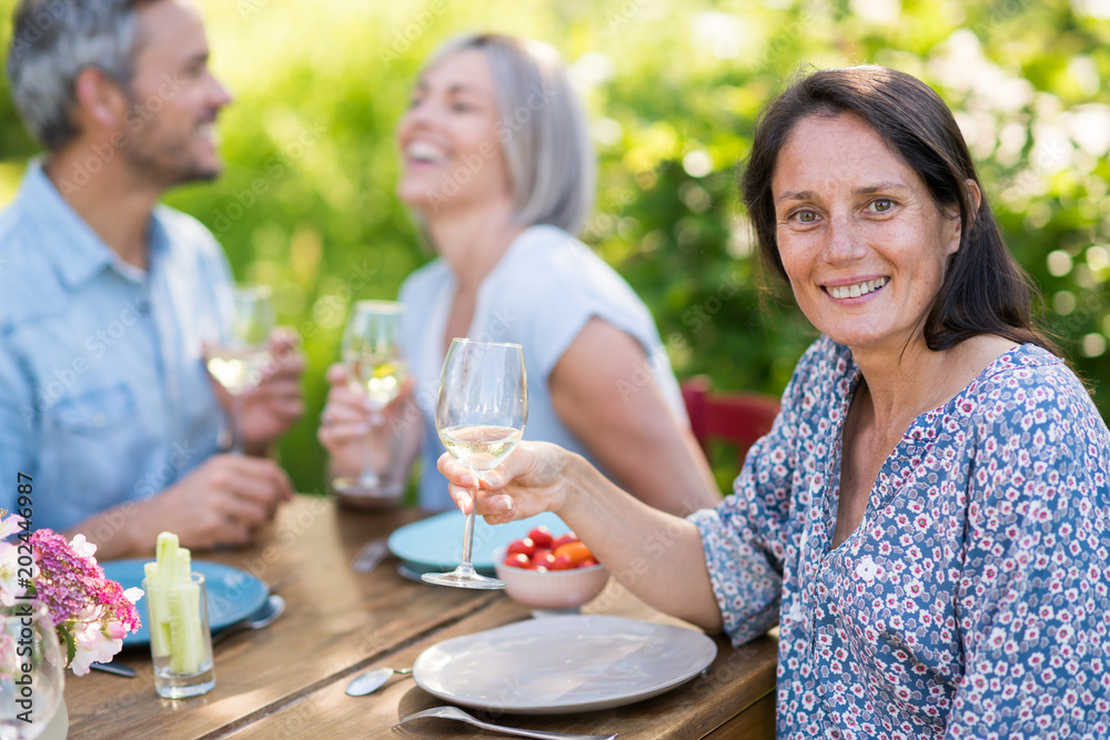 A group of friends gathered to share a meal around a table in the garden. Focus on a beautiful woman looking at the camera