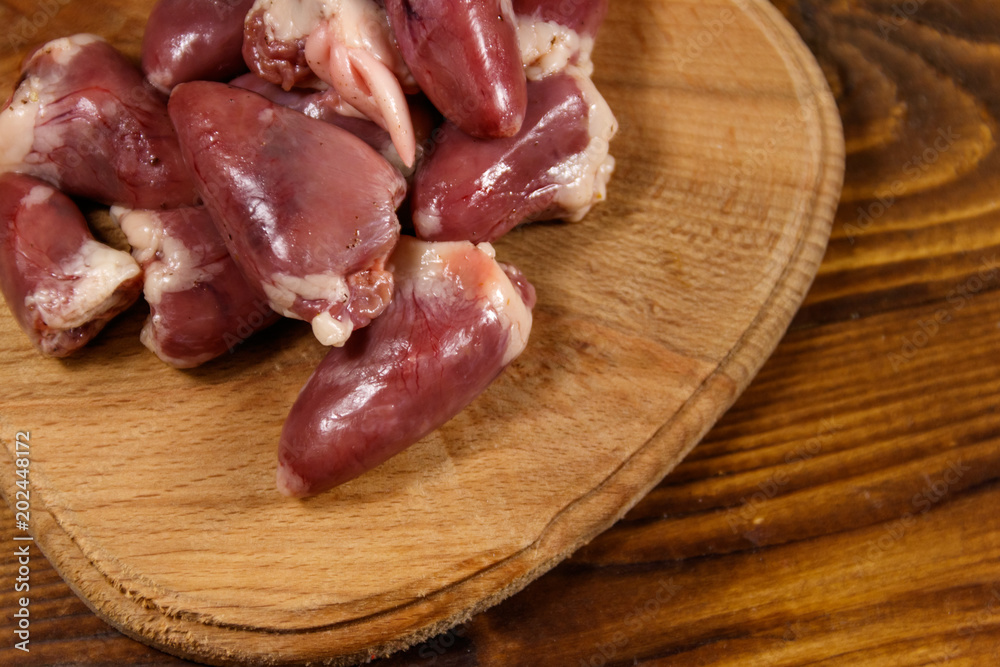 Raw chicken hearts on cutting board on wooden table Raw chicken hearts on cutting board on wooden table