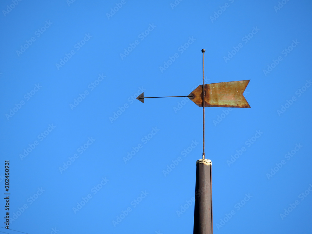Old rusty weather vane against clear blue sky. Vintage windvane on top of the tower Old rusty weather vane against clear blue sky. Vintage windvane on top of the tower