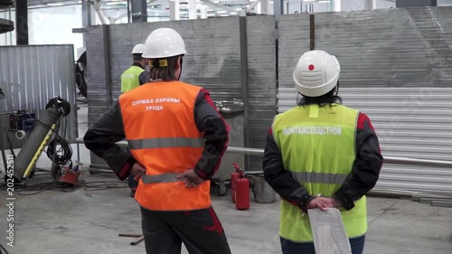 Rear view of workers talking while walking in shipping yard. Clip. Back view of two men in white safety hard hats are standing together in construction area photo