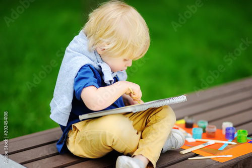 Cute little boy drawing with colorful paints in summer park
