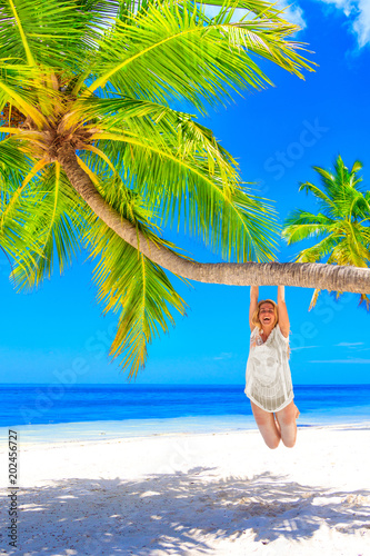 Blond woman with bikini hanging on the palm tree on the sand beach © nakedking