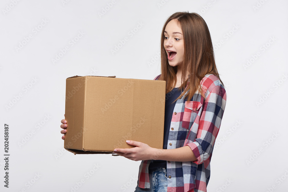Delivery, relocation and unpacking. Happy surprised young woman holding cardboard box looking at box with enthusiasm