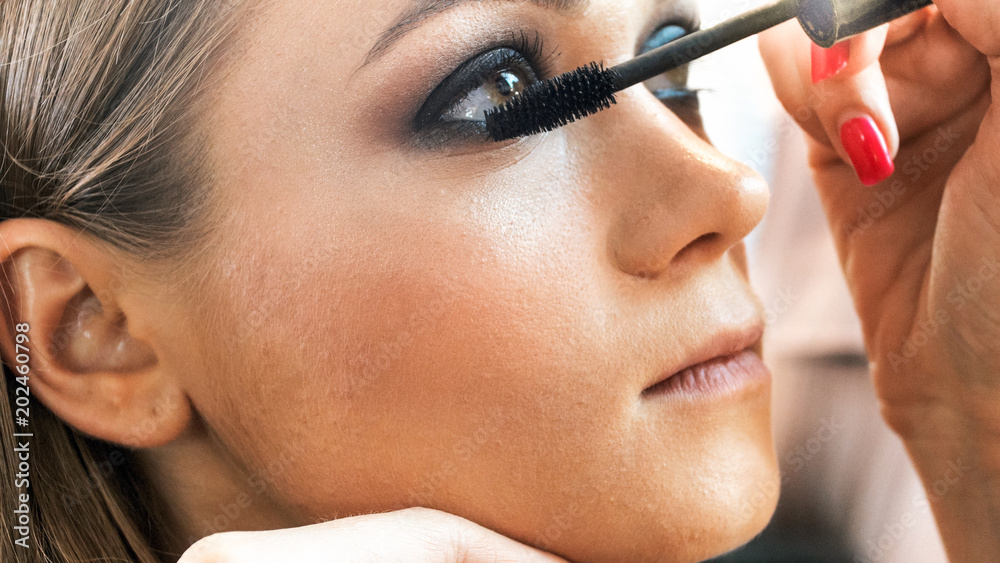 Closeup image of professional makeup artist painting eyelasshes with brush