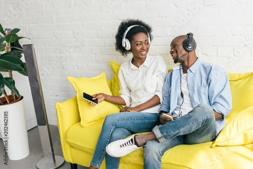 smiling african american listening music in headphones with smartphones while resting on sofa at home photo