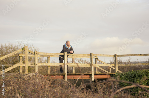 Senior man outdoors standing on a wooden bridge thinking and daydreaming 