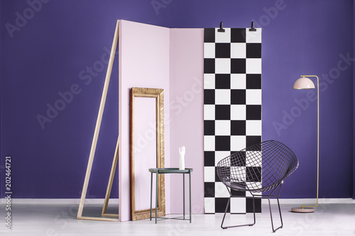 Real photo of an artistic setup in a purple interior with golden frame, pink wall and black, metal chair