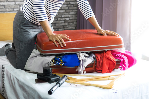 Travel and vacation concept  happiness woman packing stuff and a lot of clothes into suitcase on bed prepare for her travel and journey trip