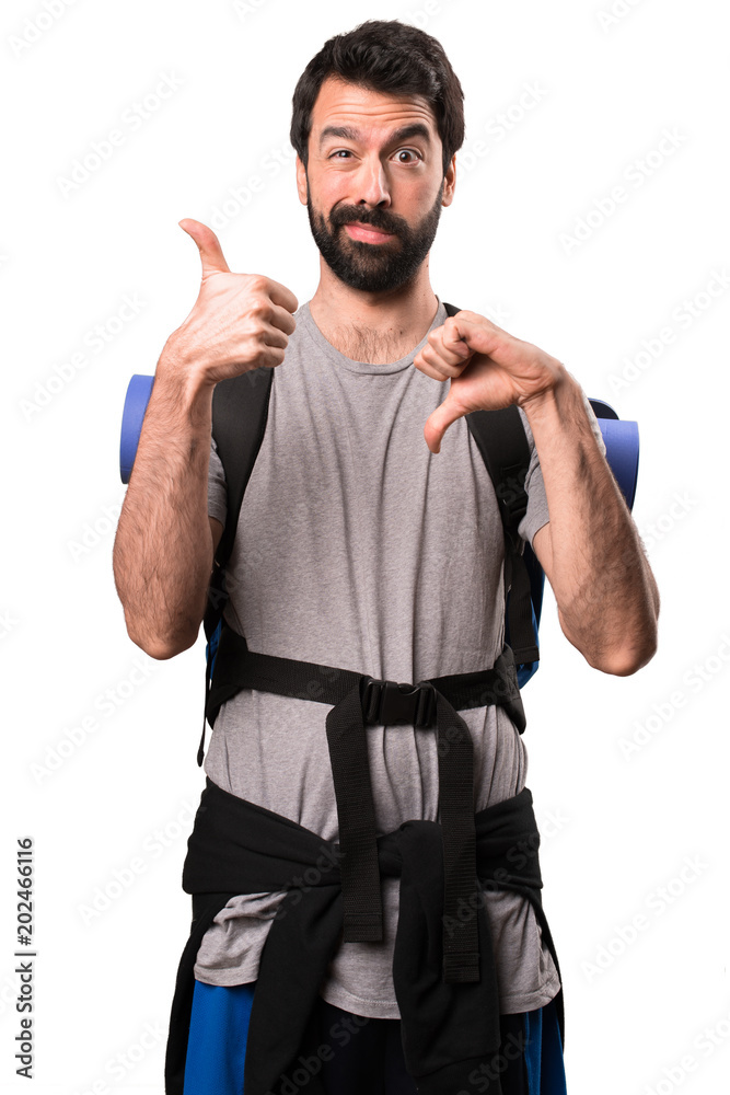 Handsome backpacker making good-bad sign on white background Handsome backpacker making good-bad sign on white background