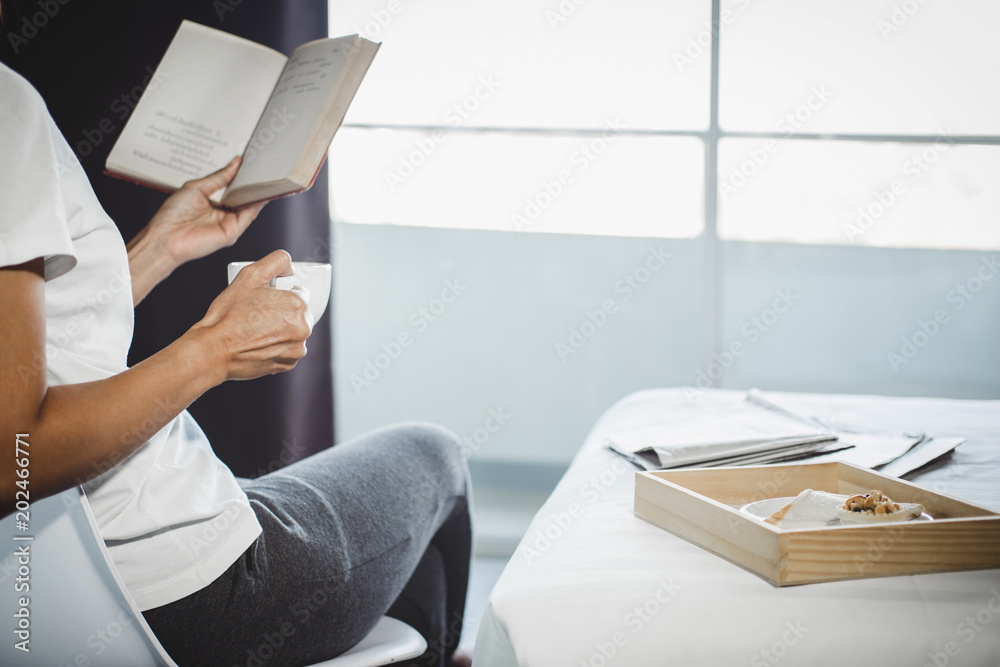 Obraz premium Young woman happiness on bedroom in enjoying reading books and newspaper in holiday with morning coffee, relaxation and recreation concept